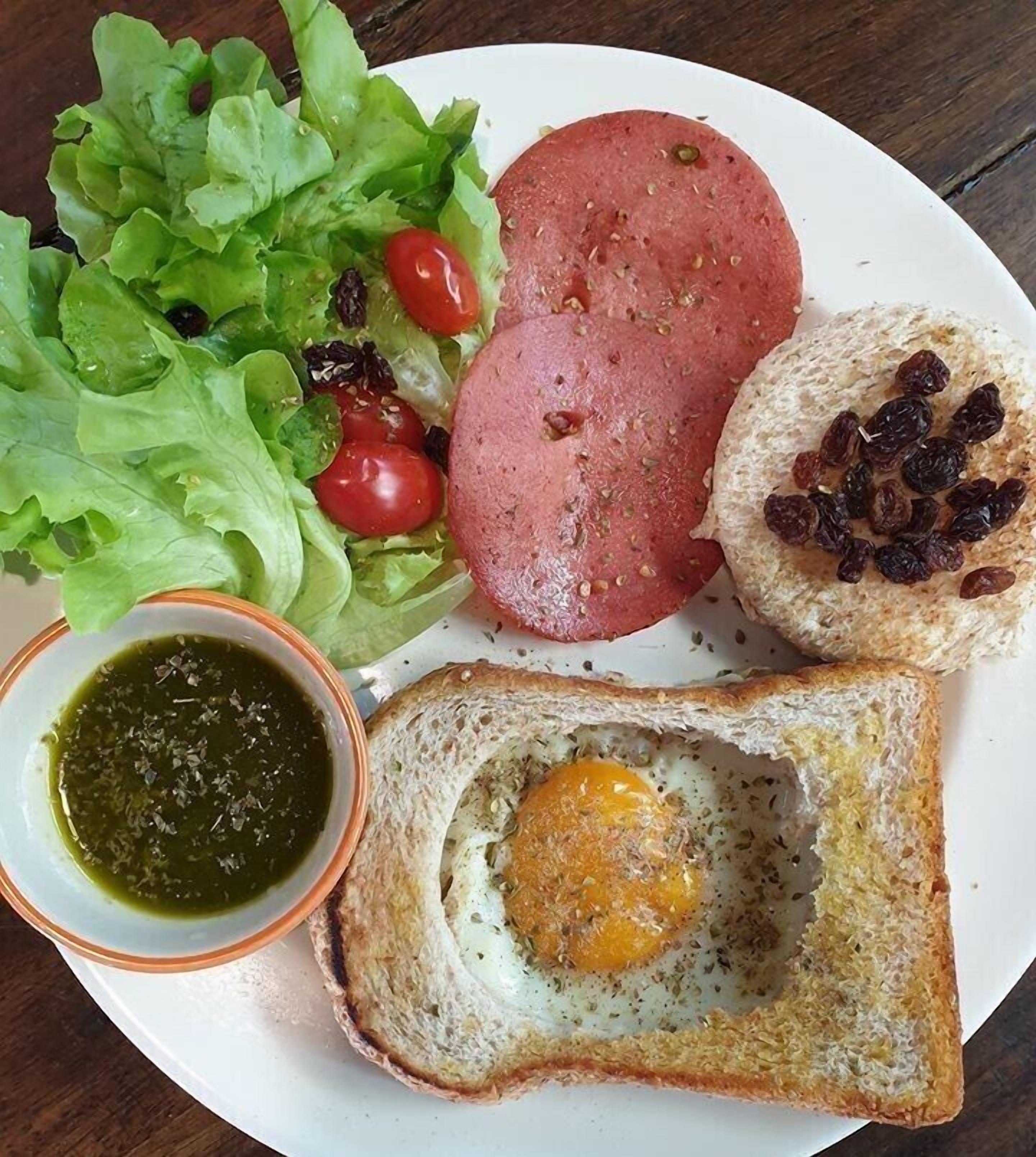 A plate with a sandwich, a slice of bread with an egg, a small bowl of sauce, and a side salad.