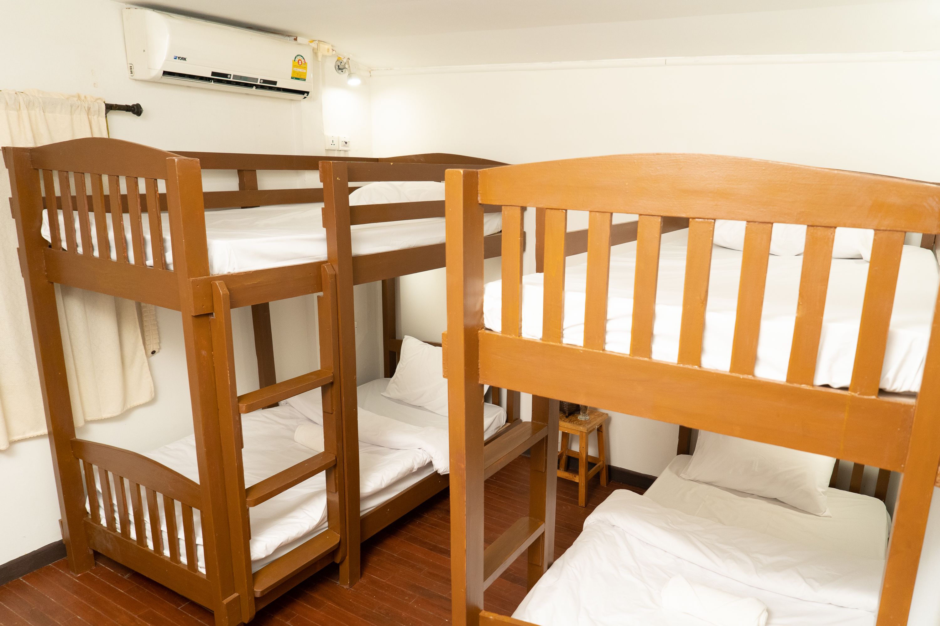 Una habitación con tres literas de madera, un taburete pequeño de madera y un equipo de aire acondicionado en la pared.