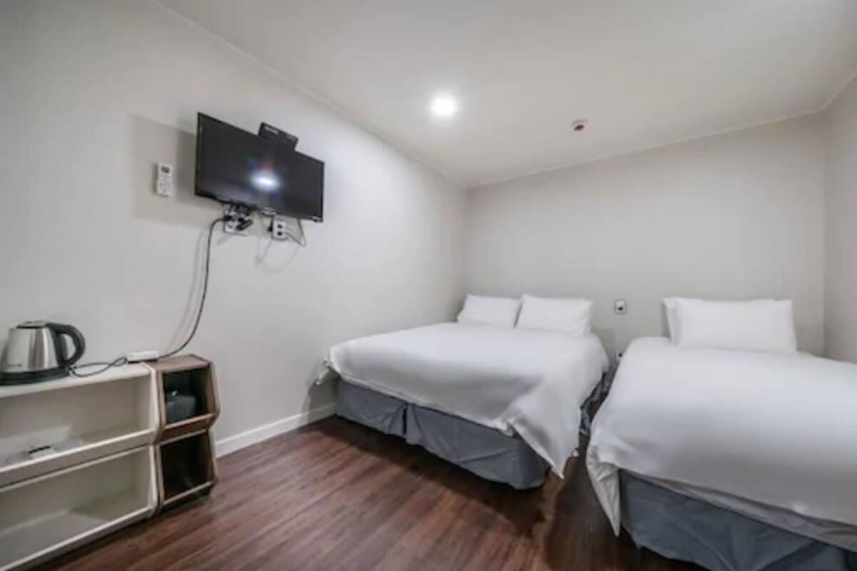 A room with two beds, a TV mounted on the wall, and a small shelf with a kettle.