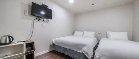 Habitación con dos camas, un televisor montado en la pared y un pequeño estante con un hervidor.