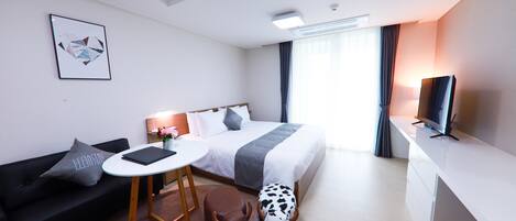 Una habitación de hotel moderna con cama, sofá, una mesita, televisor y ventana con cortinas.