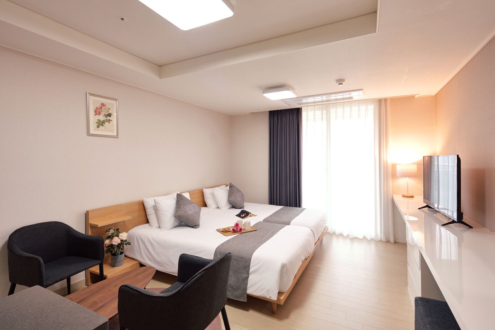 Habitació d'hotel amb un llit, dues cadires, escriptori, televisió i finestra amb cortines.