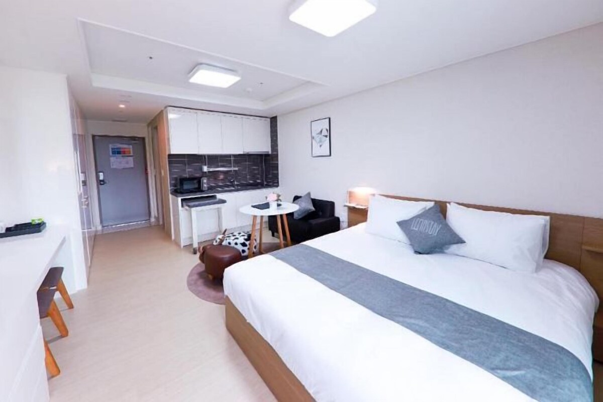 A hotel room with a bed, bedside table, and a kitchenette area.