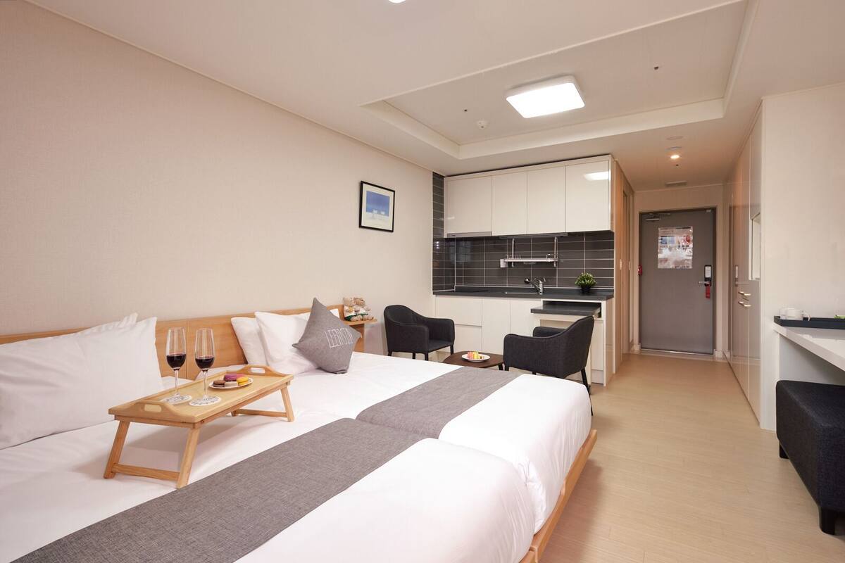 A hotel room with a bed, bedside table, and a kitchenette.