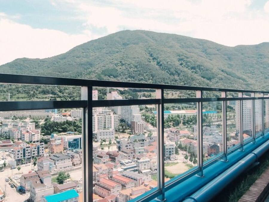 Un edificio de gran altura con fachada de vidrio, que ofrece vistas a un paisaje urbano y montañas al fondo.
