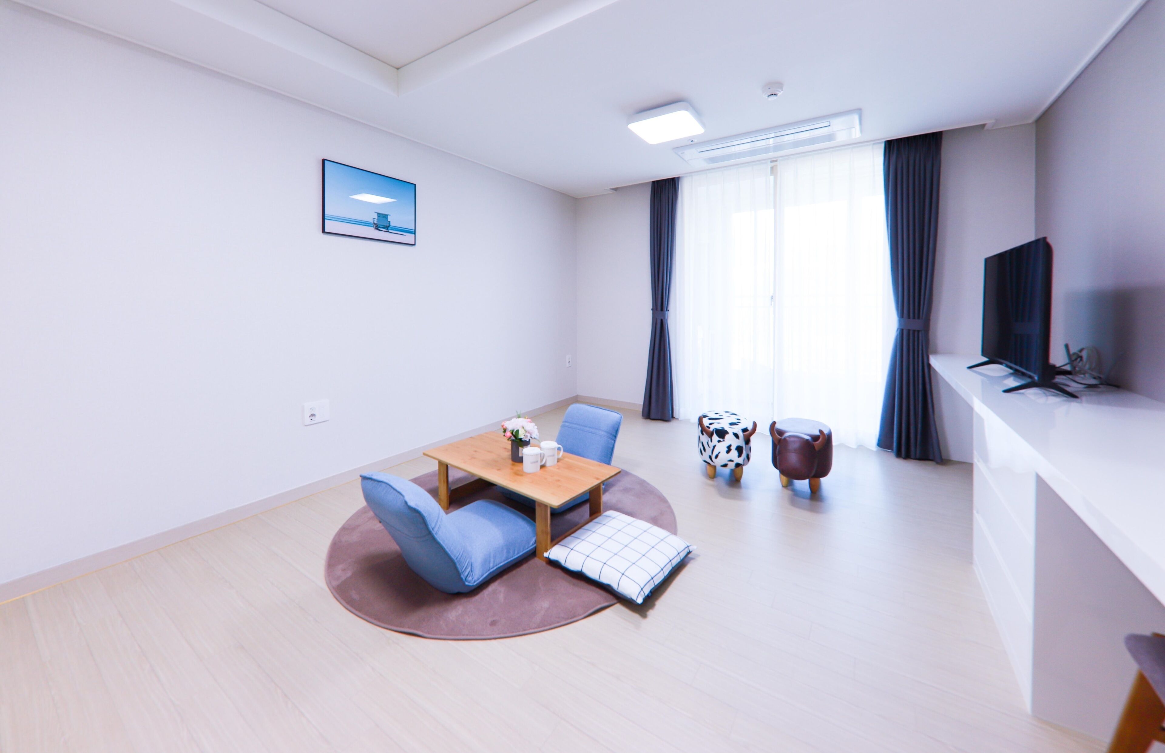 A modern hotel room with a dining area, a flat-screen TV, and a large window with curtains.
