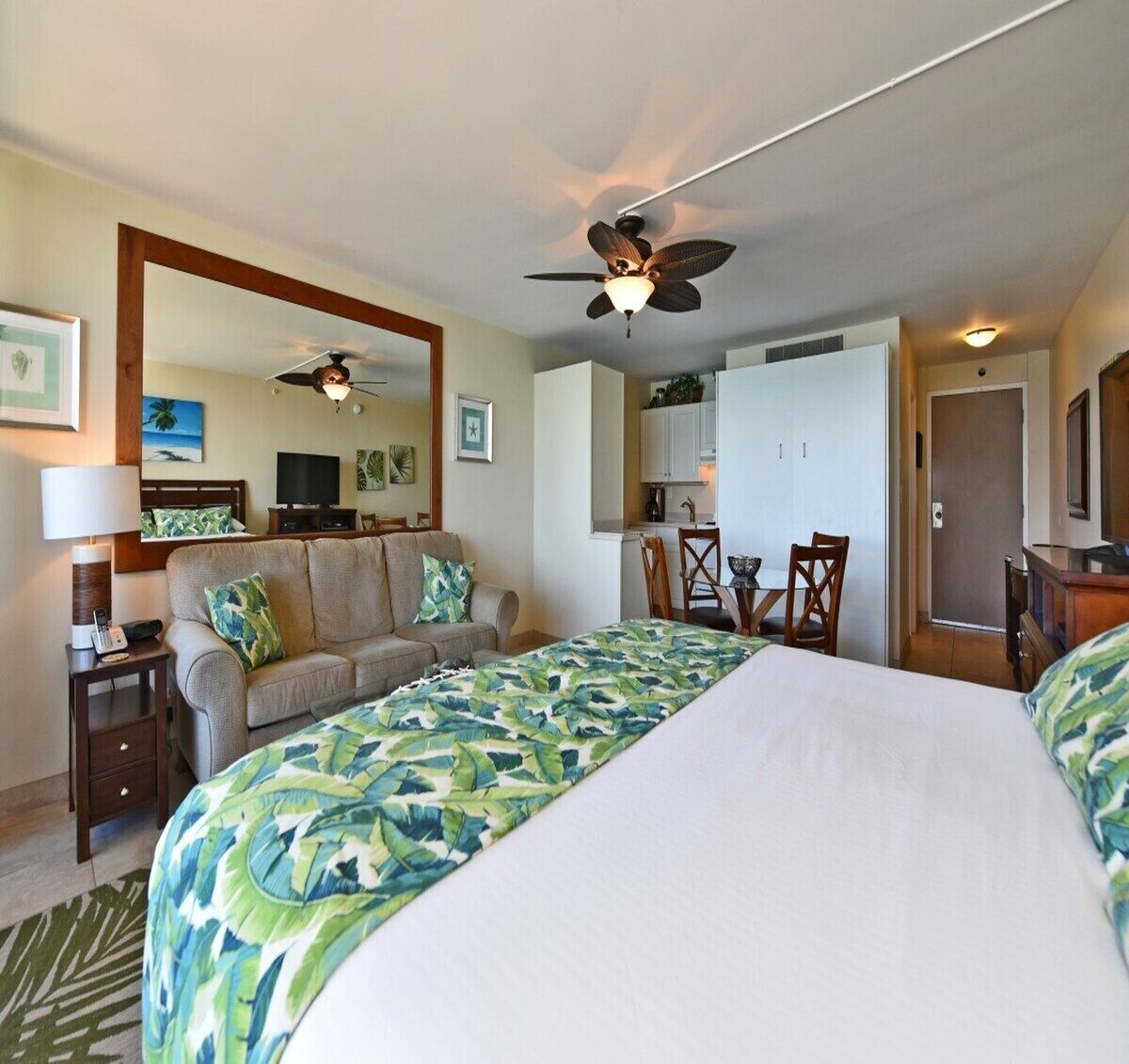 A hotel room with a large bed, a sofa, a desk, a chair, a ceiling fan, and a TV.