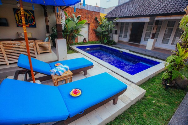 A pool area with blue lounge chairs and a small table with a flower arrangement.
