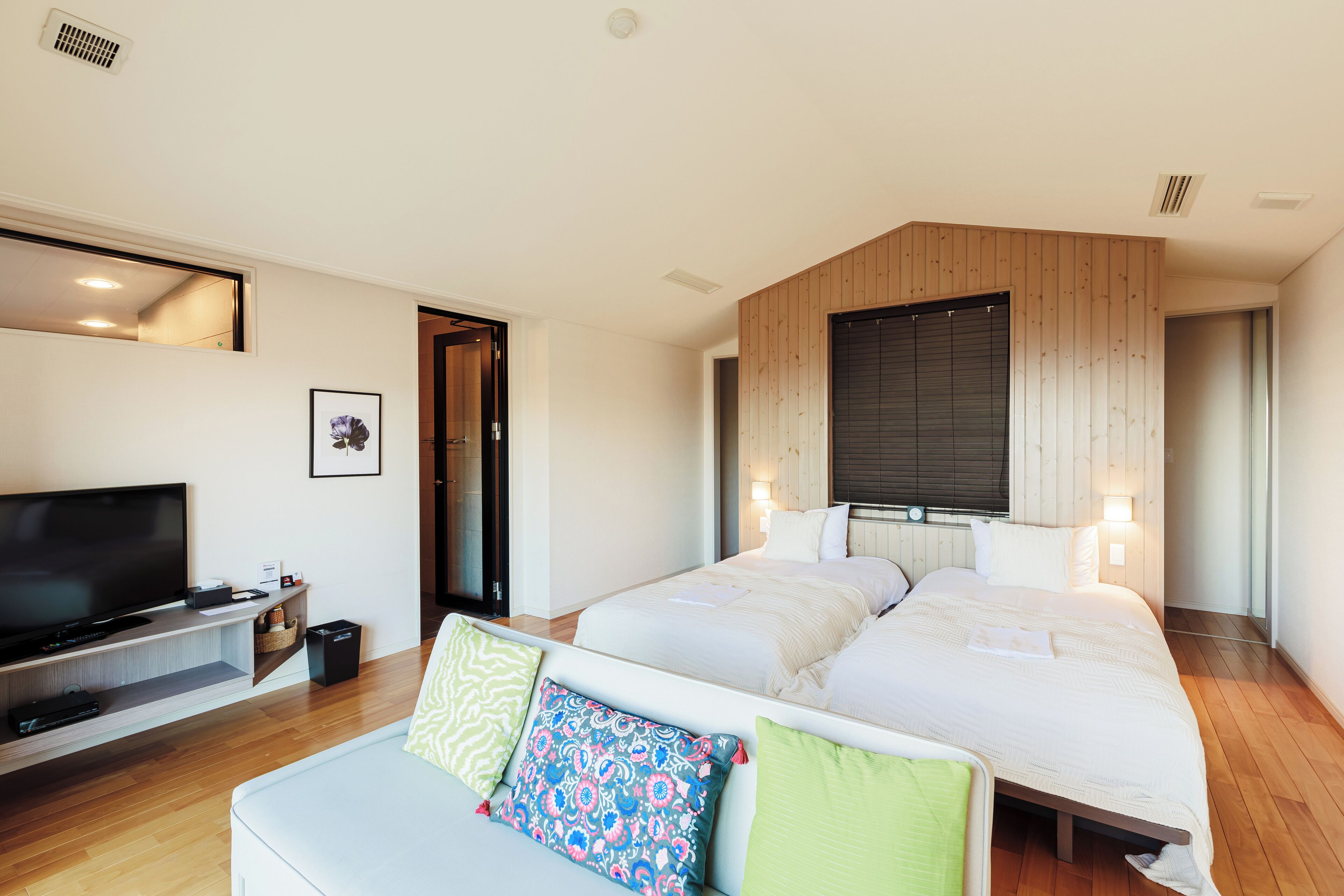 A modern hotel room with a large bed, a TV, and a wooden accent wall.