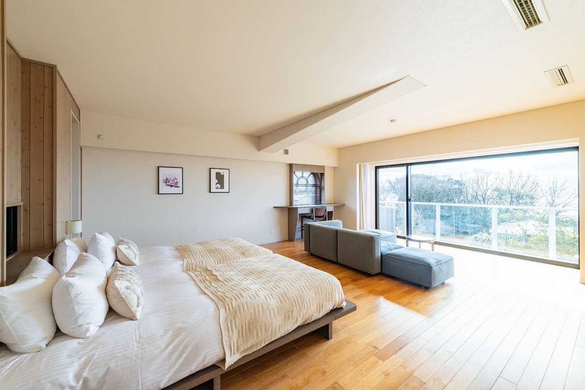 A modern bedroom with a large bed, a desk, and a view of the outdoors.