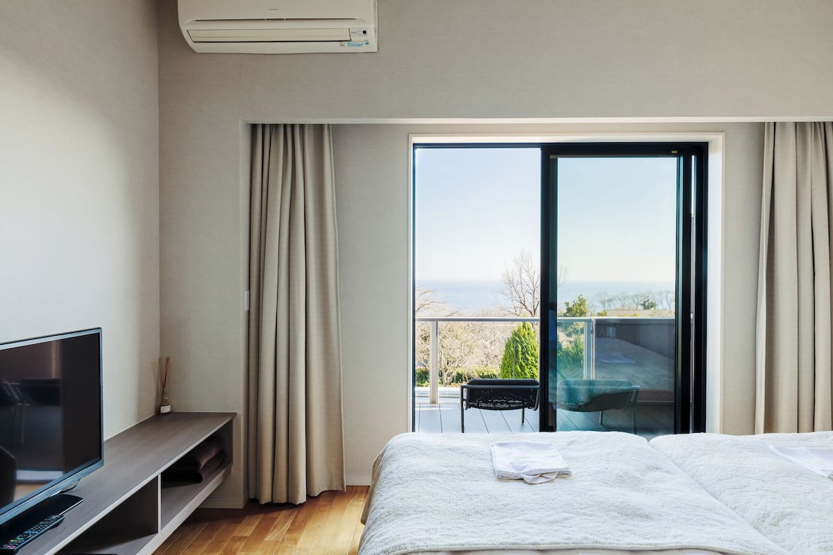 A modern hotel room with a large bed, a TV, and a balcony with a view.