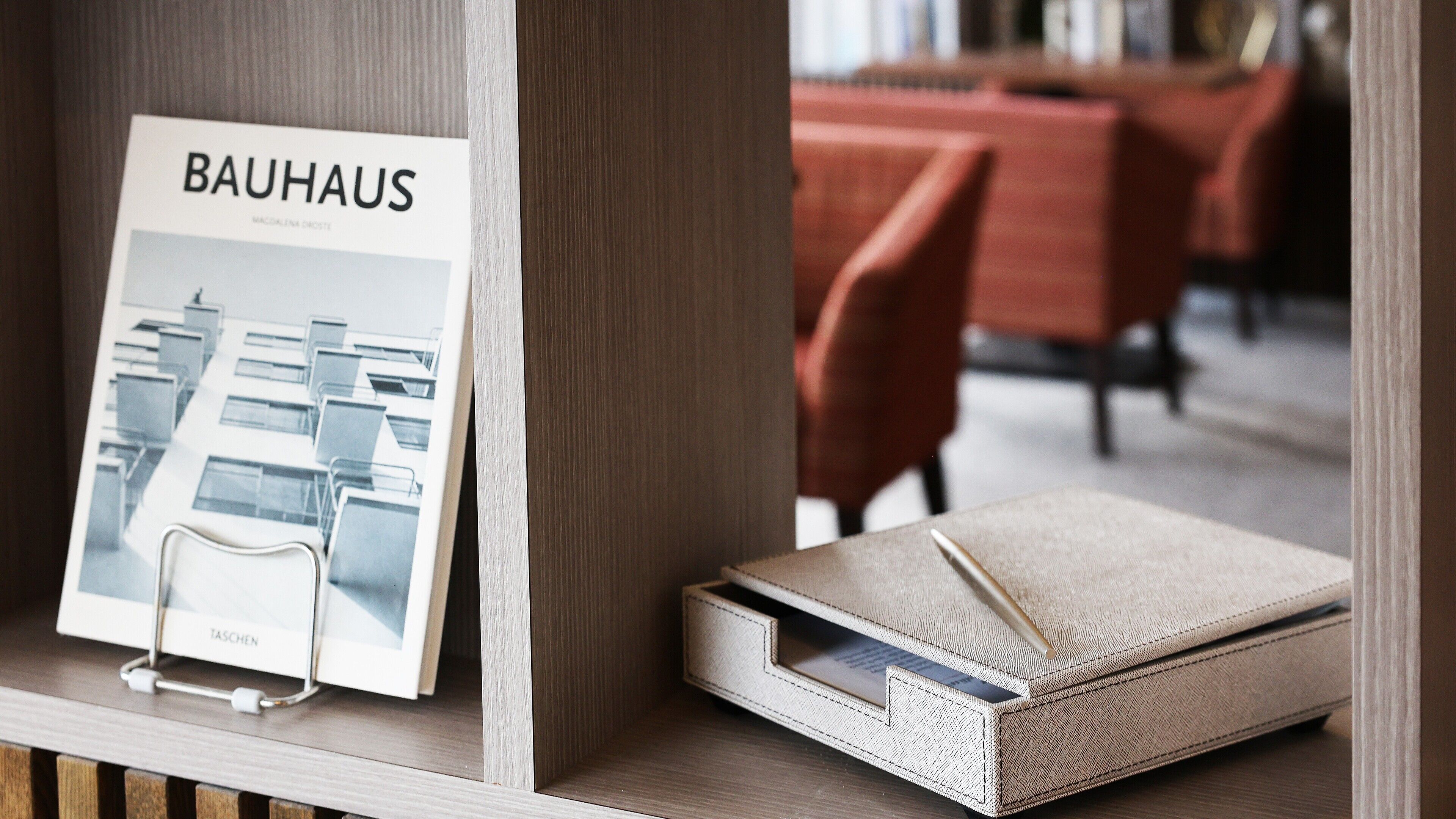 A framed Bauhaus poster, a notebook, and a pen on a shelf.