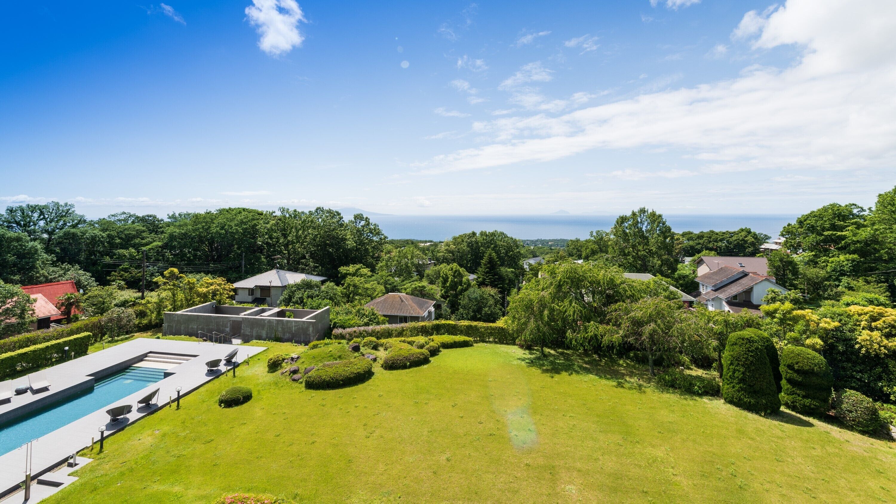 Um imóvel residencial com piscina, gramado bem cuidado e vista para o mar.