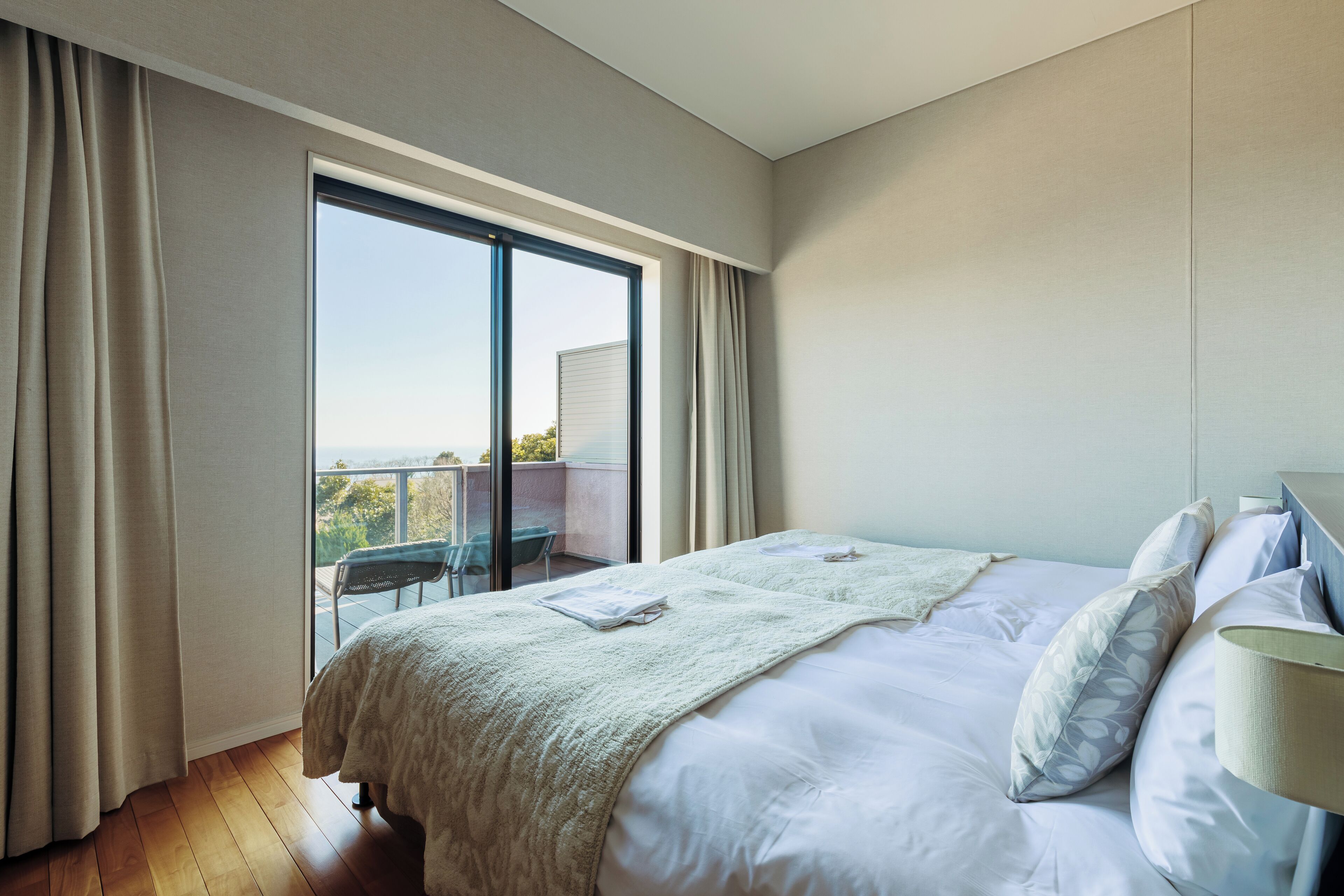 A hotel room with a large bed, a balcony with a chair, and a view of the city.