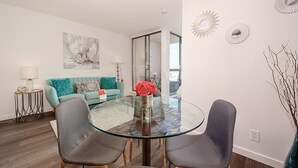 Ett modernt vardagsrum med ett matbord i glas, grå stolar, en turkos soffa och en stor, abstrakt tavla på väggen.