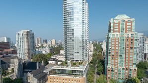 En hög byggnad med en modern glasfasad, omgiven av andra höga byggnader och en blandning av äldre arkitektur.