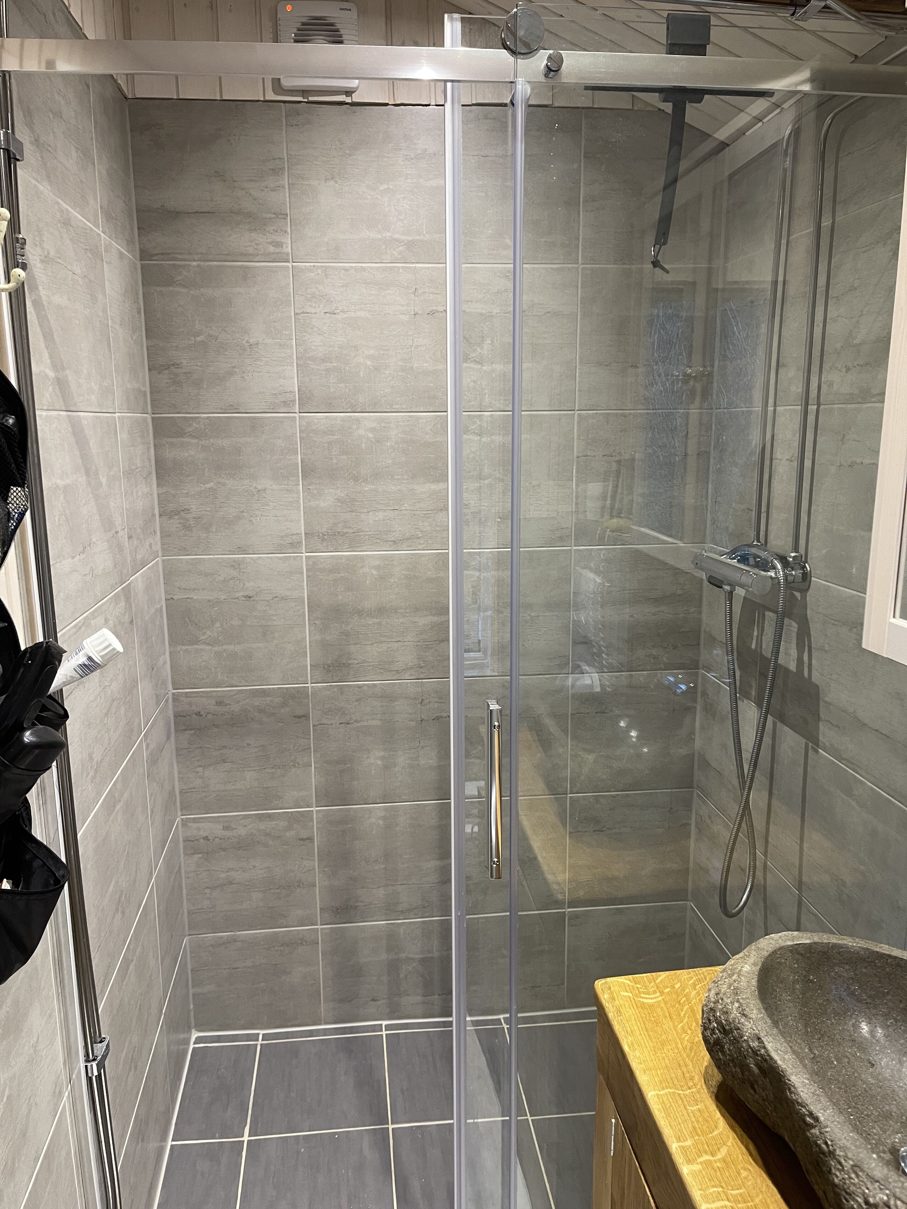 Un espace douche doté d’une porte en verre, de murs carrelés et d’un plan de toilette en bois avec un lavabo en pierre.