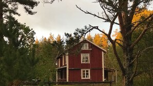 Punainen, kaksikerroksinen talo, jossa on etukuisti, ja jonka ympärillä on puita ja puinen aita.