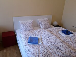 A neatly made bed with floral bedding, two pillows, and two folded towels.