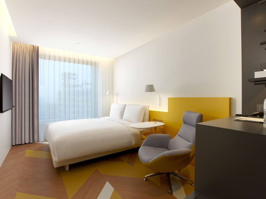 Une chambre d’hôtel moderne équipée d’un lit, d’un bureau, d’une chaise, d’une télévision et d’une fenêtre avec des rideaux.