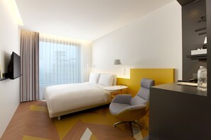 A modern hotel room with a bed, a desk, a chair, a TV, and a window with curtains.
