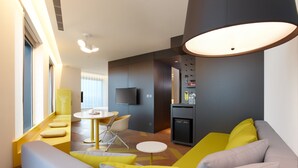 A modern living room with a sofa, yellow cushions, a dining table with chairs, a flat-screen TV mounted on the wall, and a kitchen area with a refrigerator. - The Place Taipei (Taipei)