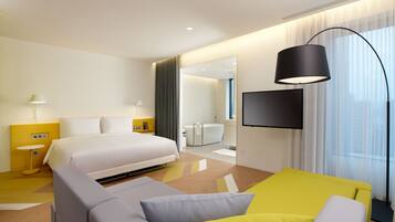 Een moderne hotelkamer met een groot bed, een bank, een televisie en een badkamer zichtbaar door een open deur.