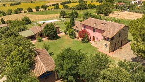 A stone house with a tiled roof, surrounded by green fields and trees.