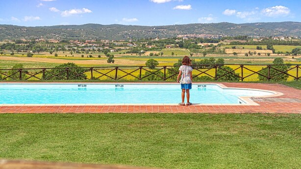 A person standing by a rectangular pool with a view of a rural landscape and hills in the background.