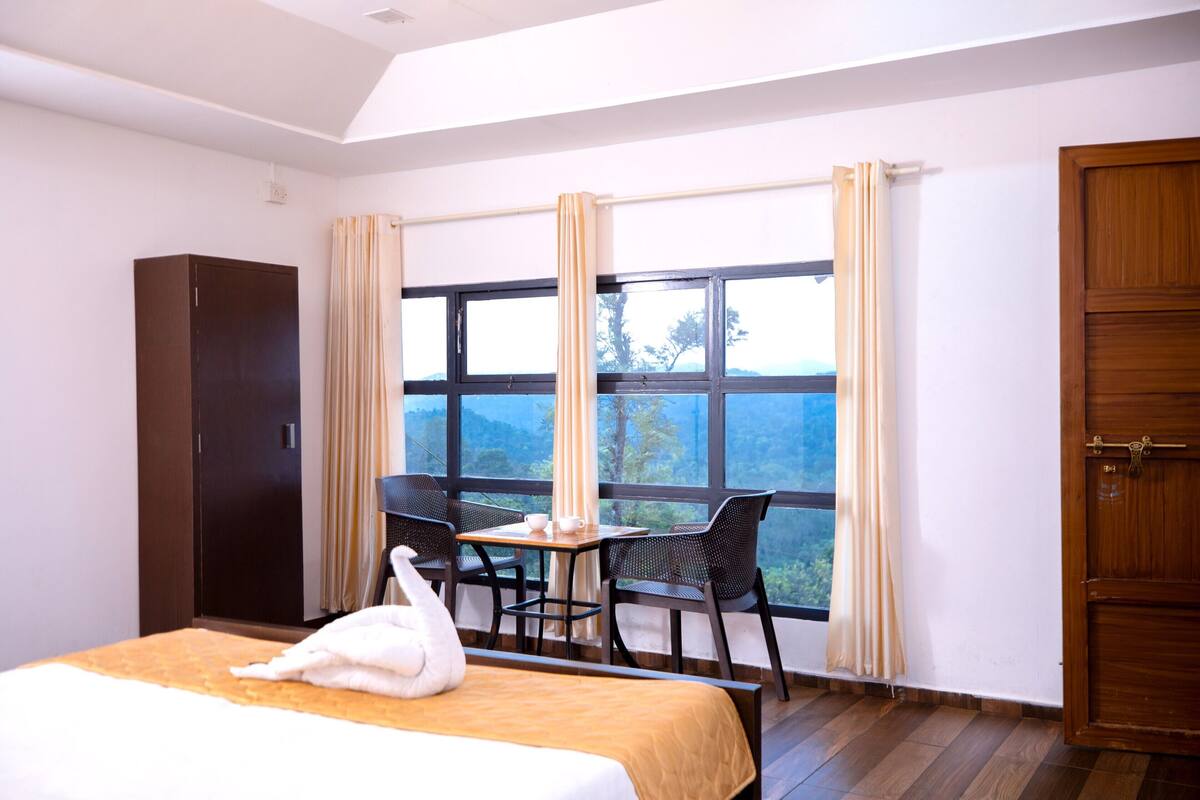 Una habitación de hotel con cama, una mesa con sillas, una ventana con cortinas y un armario.