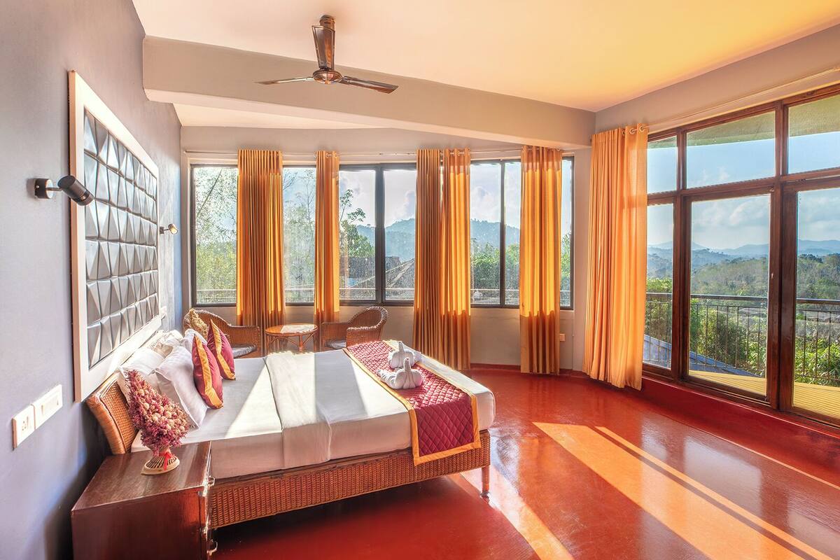 Un dormitorio amplio con una cama grande, un ventilador de techo y varias ventanas que ofrecen vistas panorámicas.