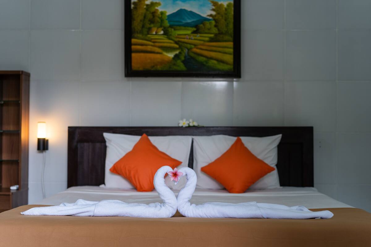 Une chambre d’hôtel avec un lit, deux oreillers orange, un tableau au mur et des serviettes disposées sur le lit.