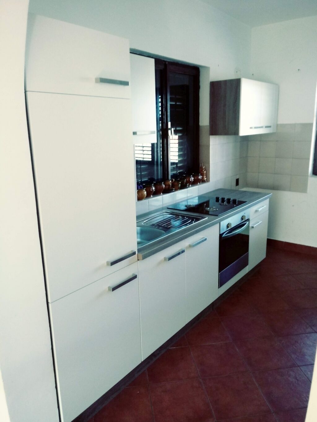 Una cocina moderna con gabinetes blancos, una estufa de acero inoxidable y un ventanal con persianas.