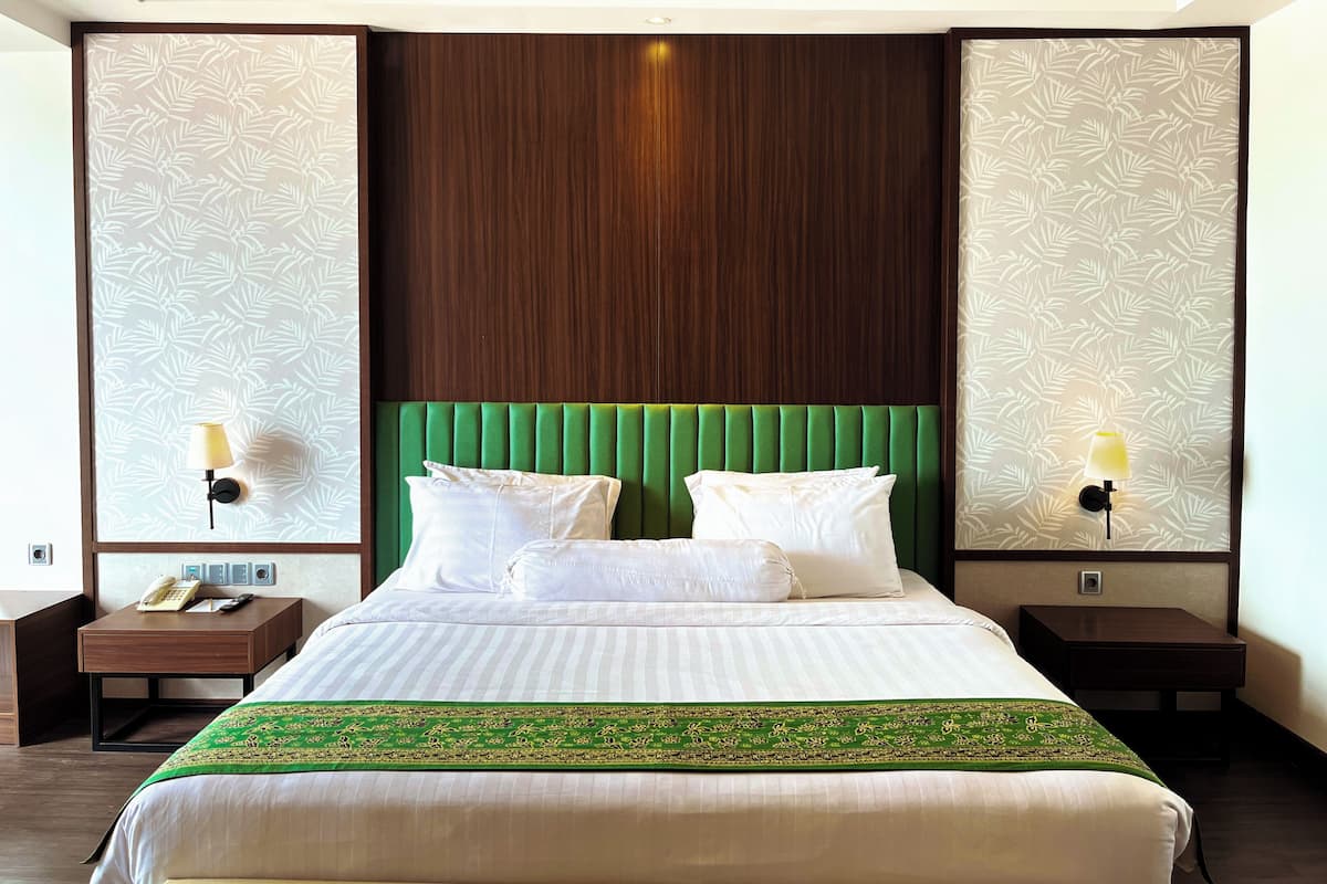 A hotel room with a large bed, two bedside tables, a green upholstered headboard, and patterned wallpaper.