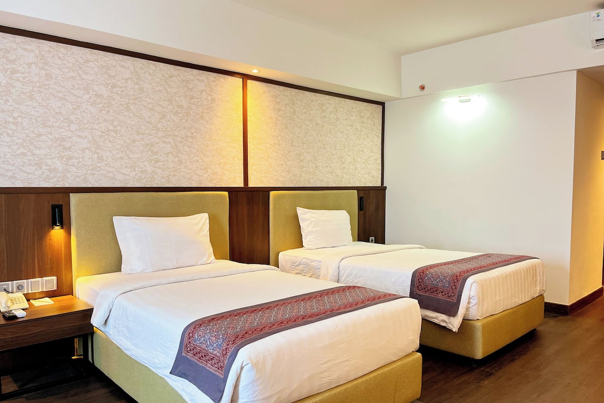 A hotel room with two beds, wooden headboards, a patterned wall, and a nightstand with a phone.