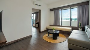 A modern living room with a sofa, a round coffee table, a view of the outdoors, and a television. - Wiltop Hotel (Jambi)
