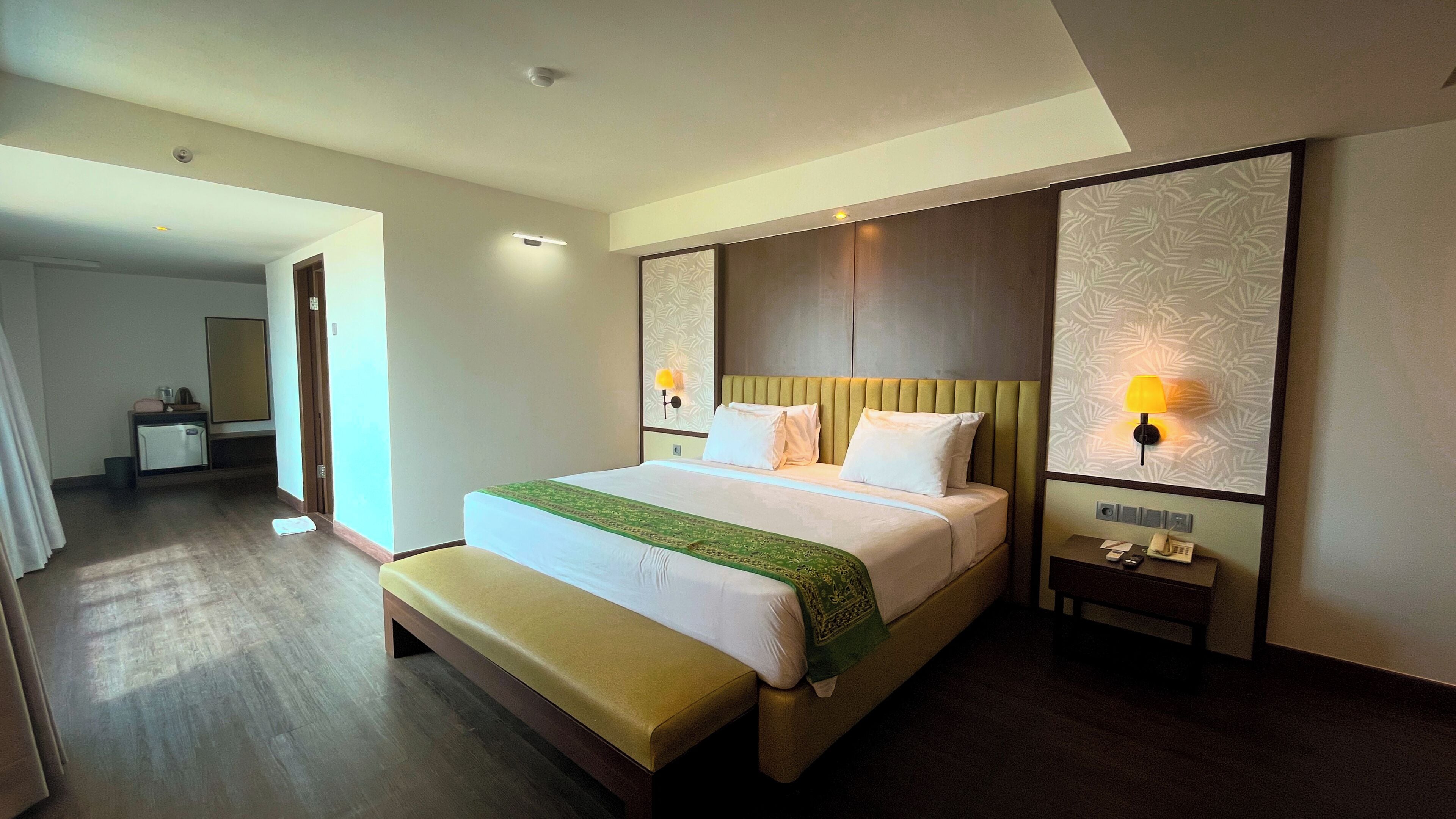 A hotel room with a bed, bedside tables, a bench, a desk, and a mirror.
