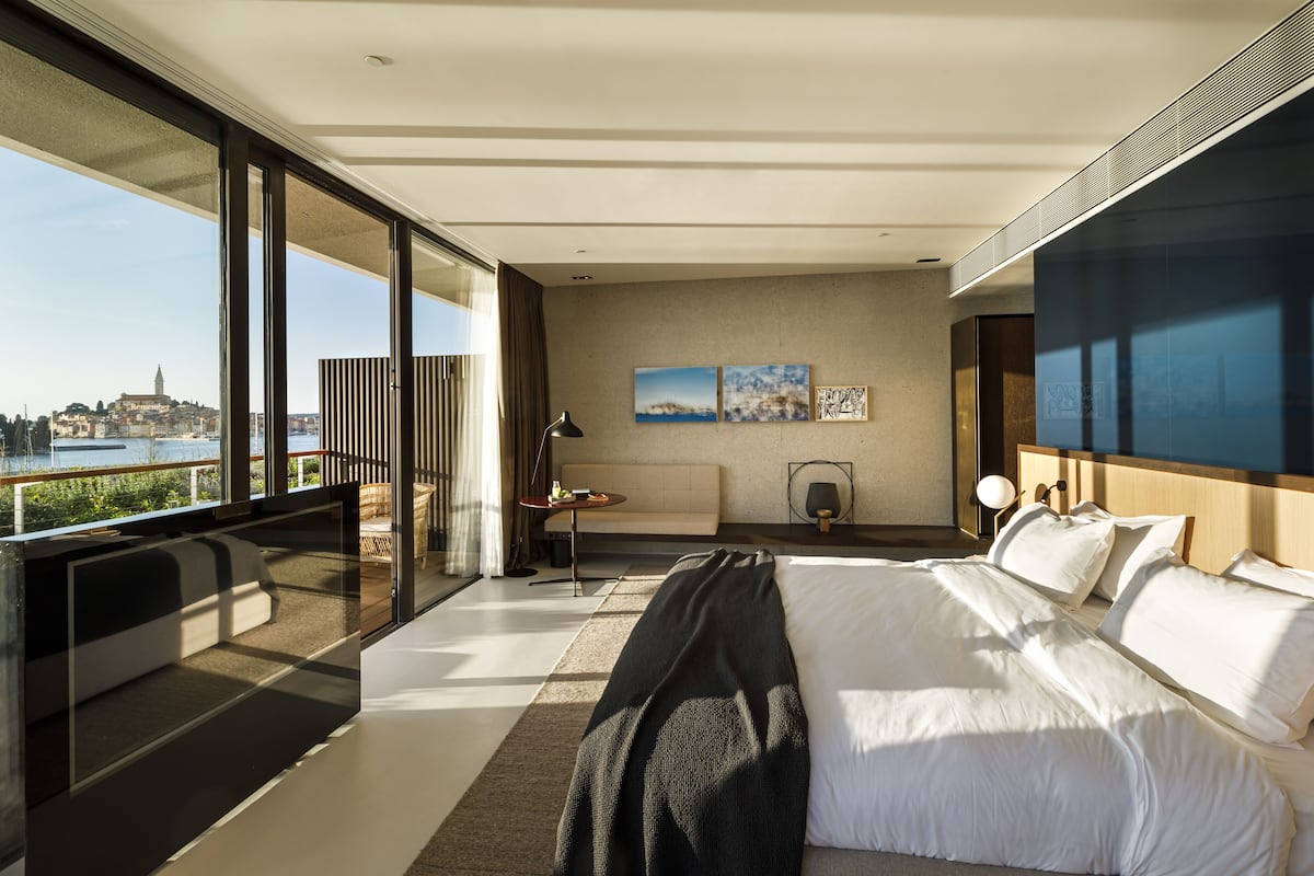 Una habitación de hotel moderna con una cama grande, vistas a la ciudad y un balcón con mesa y sillas.