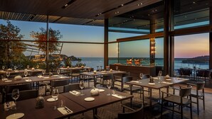 Ein Restaurant mit gedeckten Tischen, große Fenster mit Blick auf das Meer und die Stadtlandschaft.