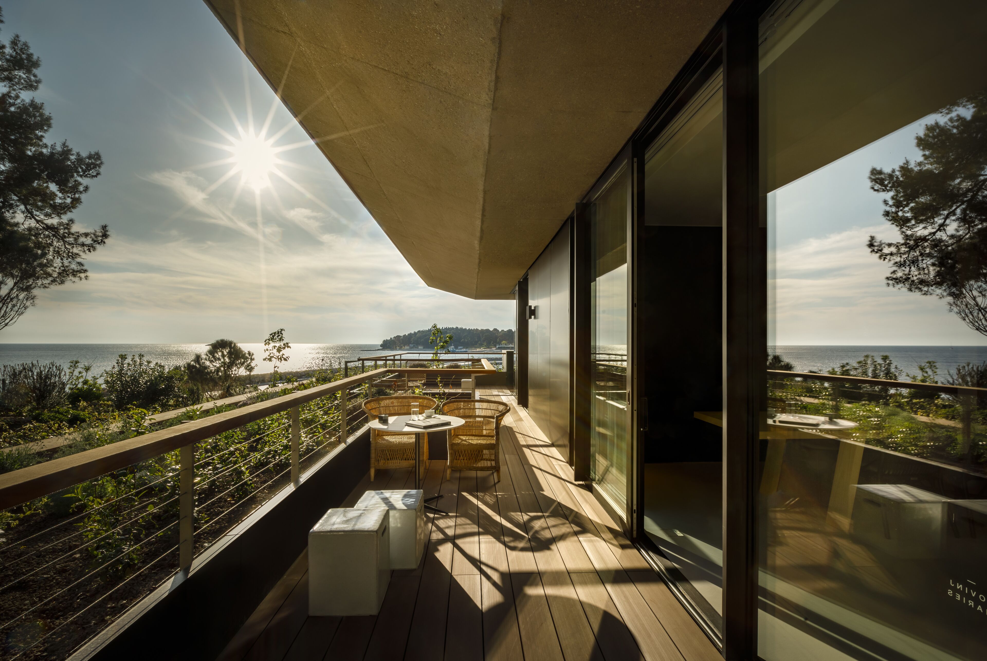 A wooden deck with outdoor furniture, a glass door, and a view of the sea and distant land.