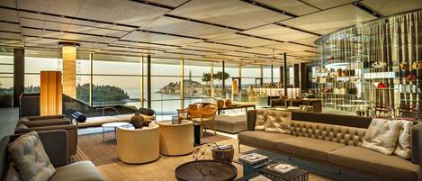 Un vaste espace de vie doté d’une grande fenêtre offrant une vue sur la ville, de sièges confortables et d’une bibliothèque au design moderne.