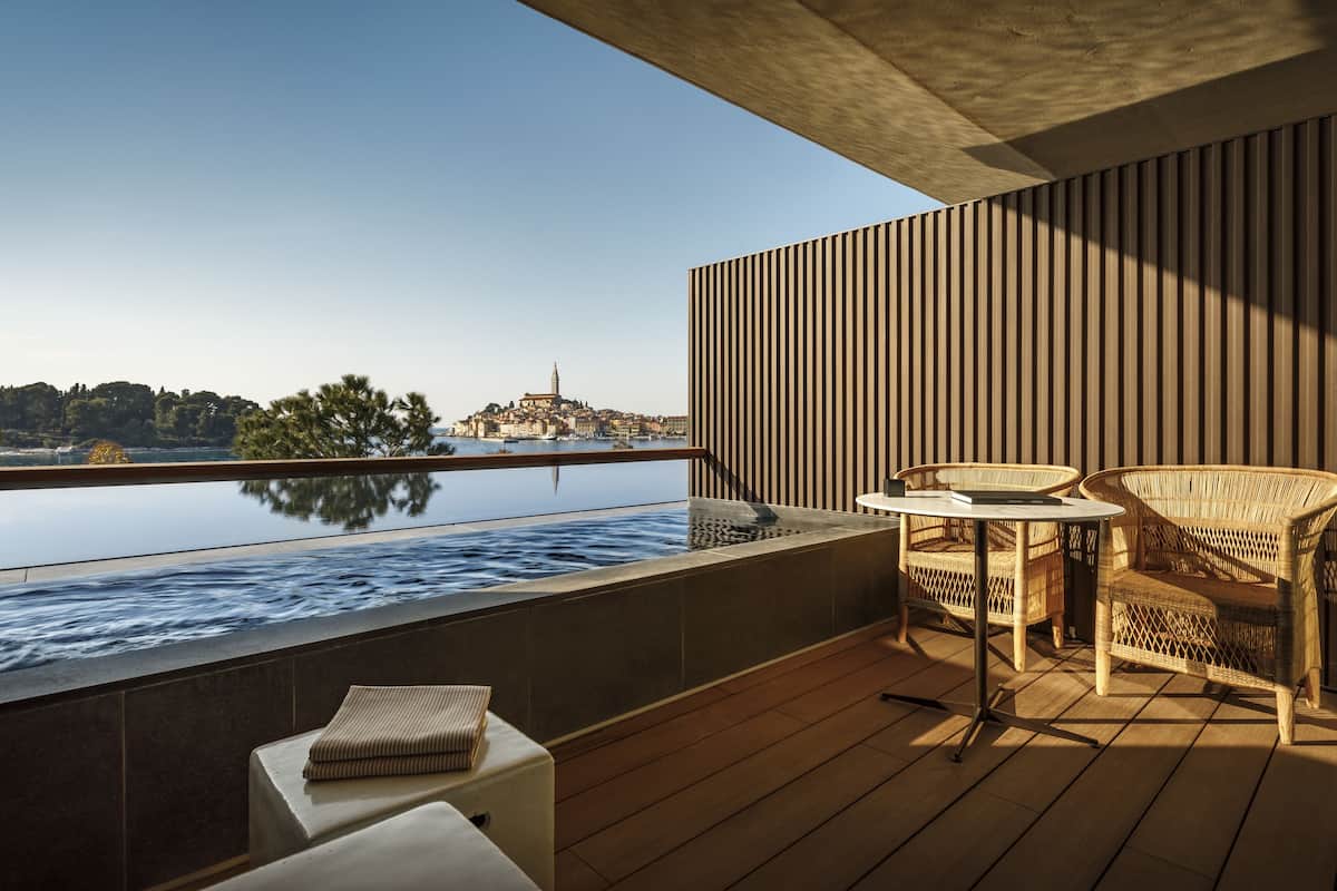 Un balcón con vista a un paisaje urbano, una piscina y mobiliario de mimbre.
