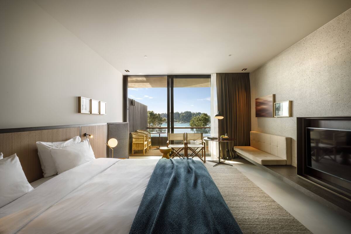 Una habitación de hotel moderna con una cama grande, televisión y balcón con vistas al exterior.