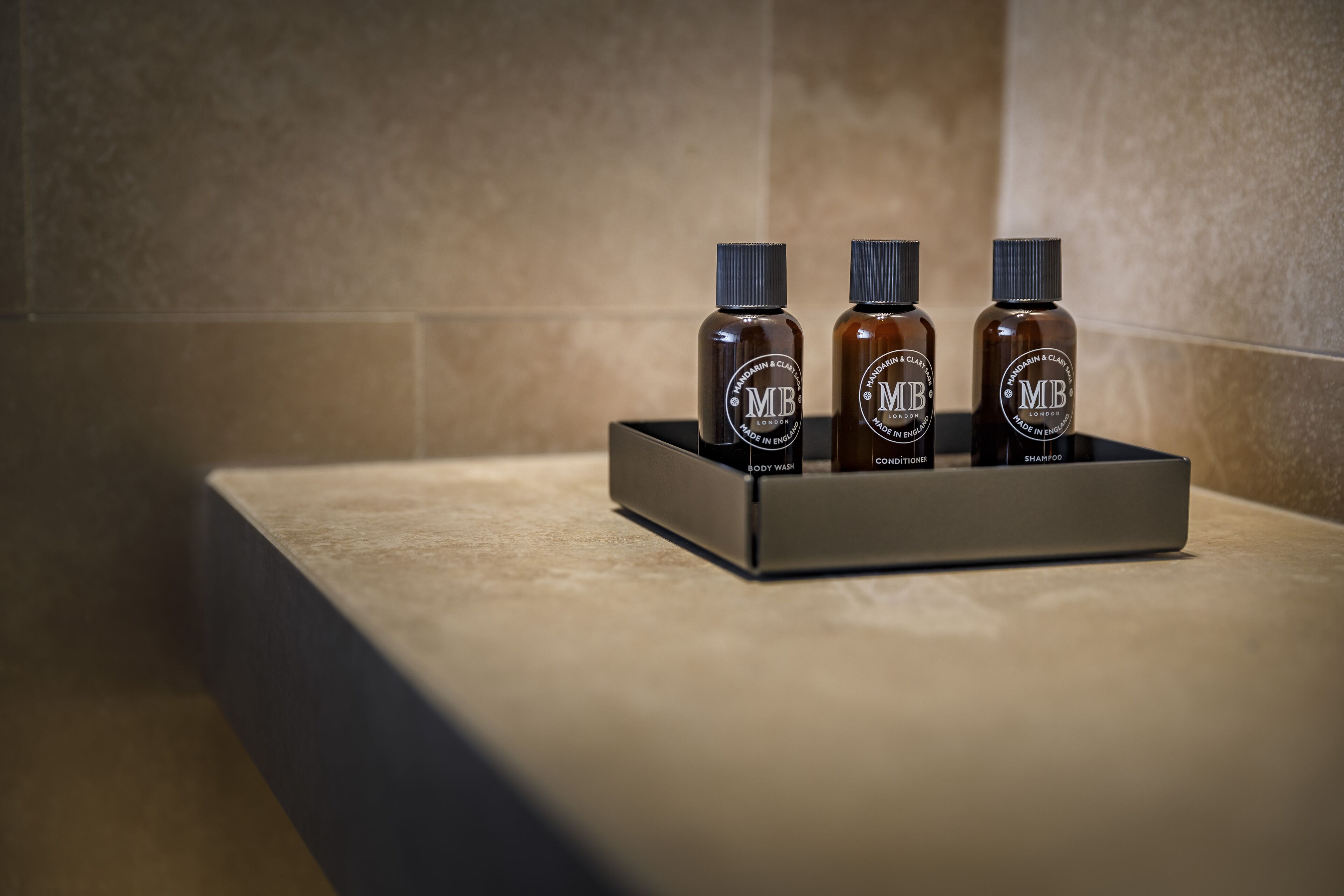 Three bottles of MB body wash, conditioner, and shampoo on a tray.