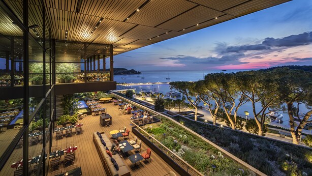 Eine Dachterrasse mit Außenmöbeln, Blick auf das Meer und einer Holzbalkendecke.