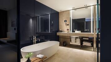 A modern bathroom with a freestanding bathtub, a large mirror, and a wooden stool with a plant.