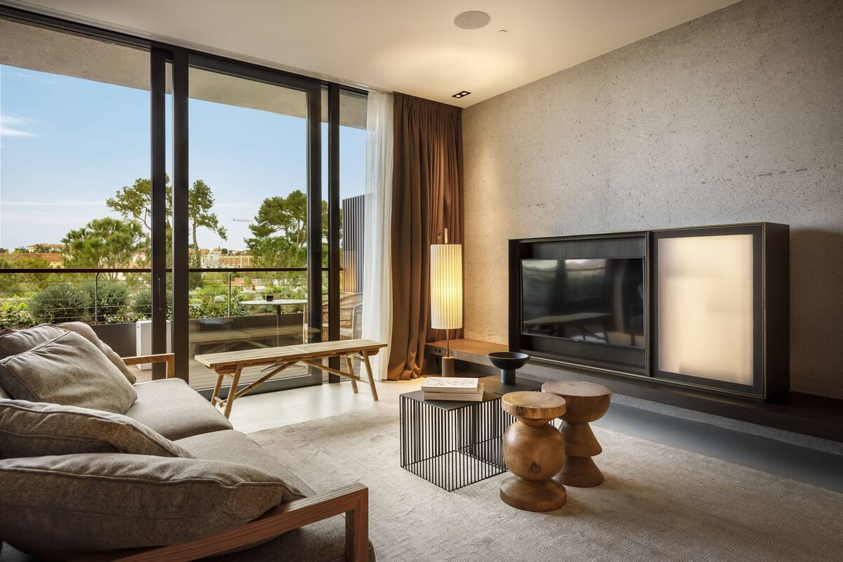 Una sala de estar moderna con sofá, mesa de centro, televisor y vistas al verdor exterior.