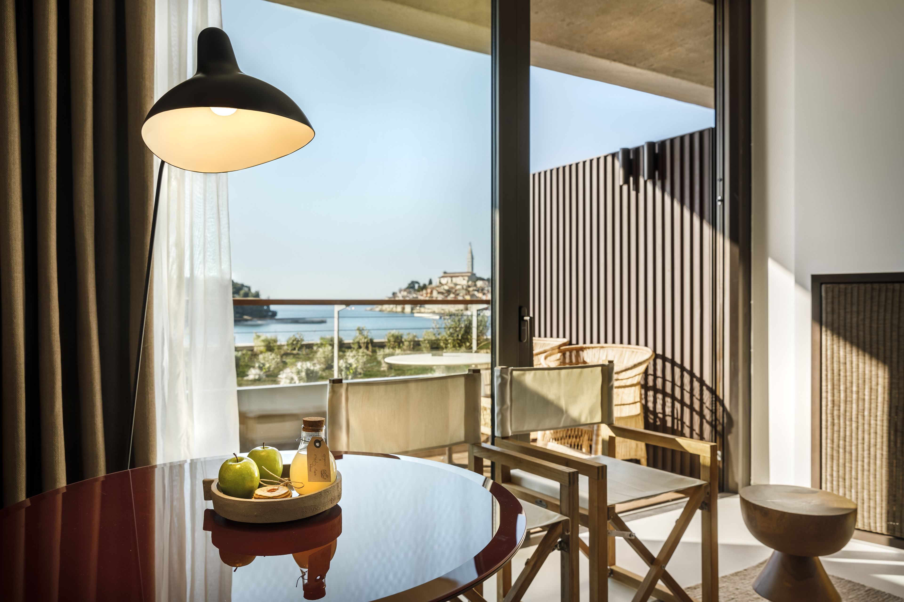 A modern room with a dining table, chairs, a lamp, and a view of a cityscape and water.
