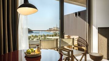 A modern room with a dining table, chairs, a lamp, and a view of a cityscape and water.