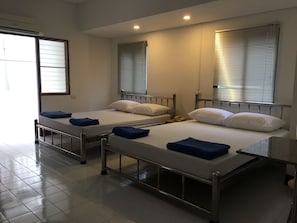 A hotel room with two single beds, each with a metal frame and white bedding. There are two windows with blinds, and the room has a tiled floor. - AP Aparment (Krathum Baen)